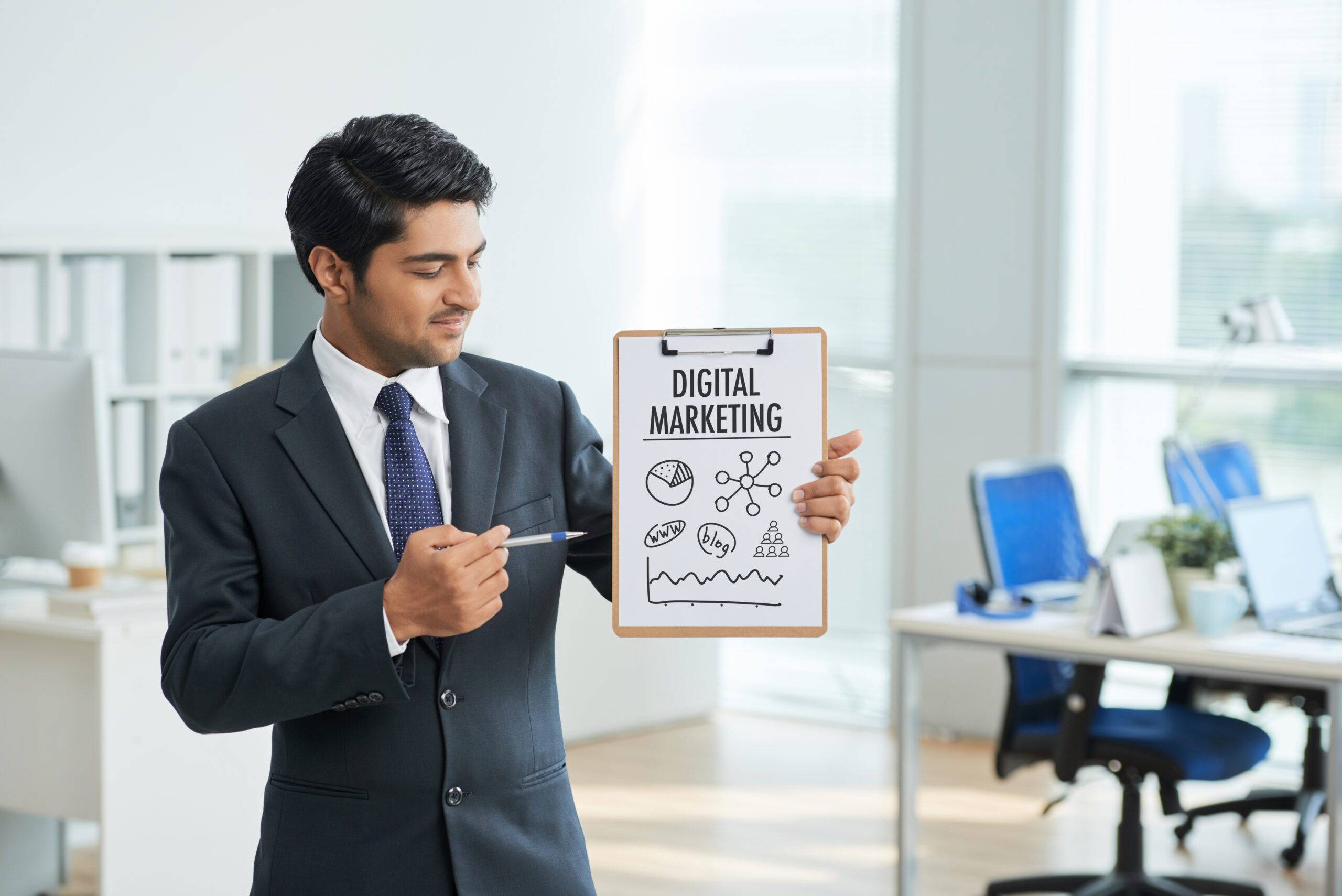 man-suit-standing-office-with-clipboard-pointing-poster-with-words | UpRango Top Digital Marketing Agency