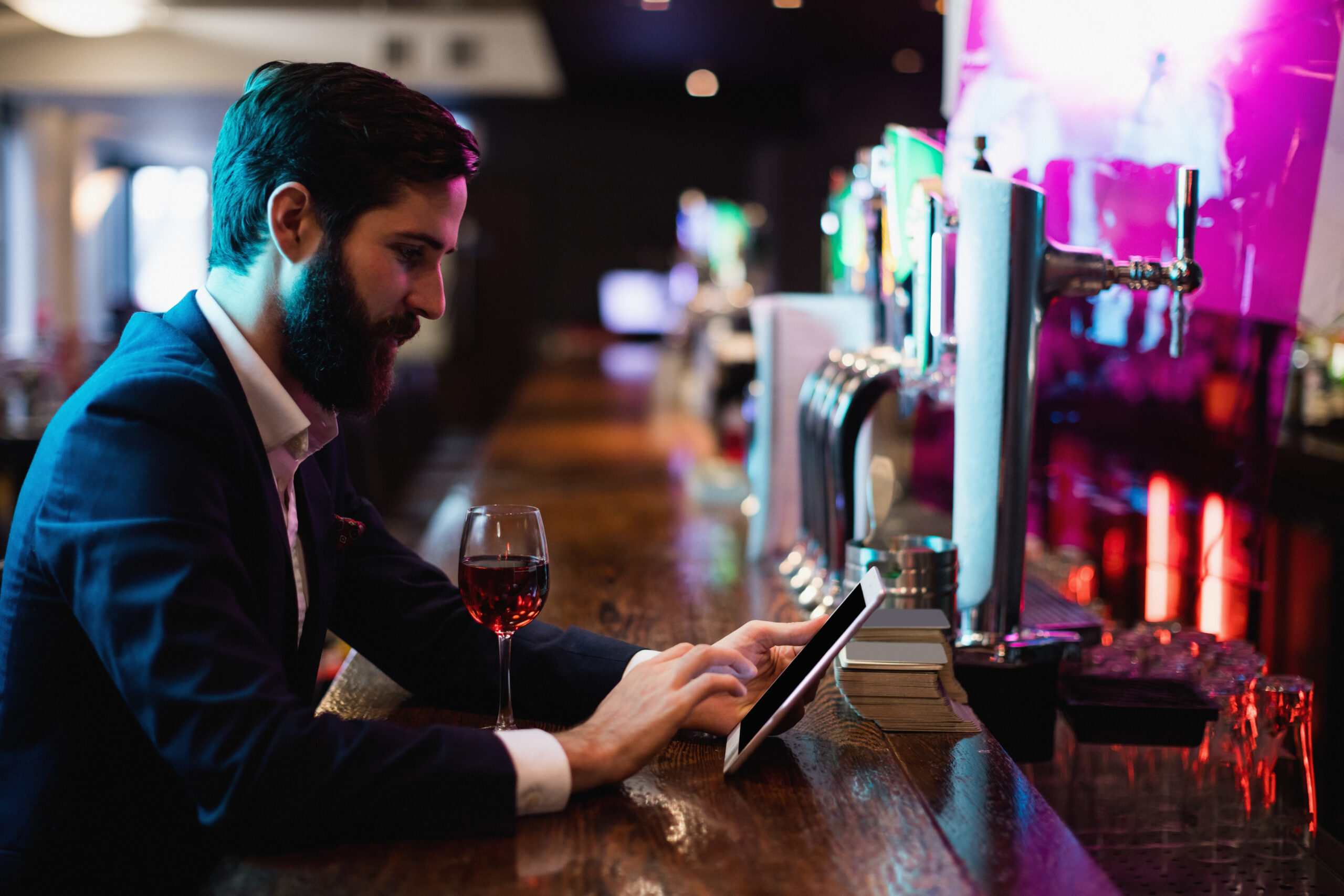 Businessman using digital tablet with wine glass on counter in bar | UpRango Casino SEO Services